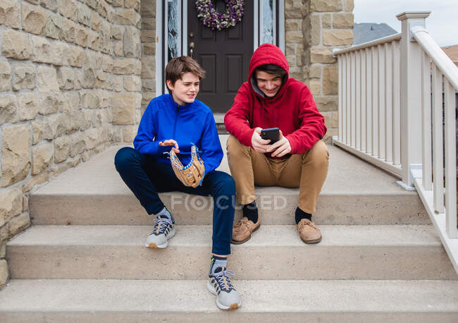 Dos adolescentes sentados y hablando en los escalones de una casa. - foto de stock