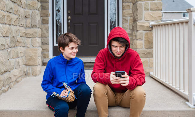 Two teenage boys sitting and talking on the front steps of a house. — Stock Photo