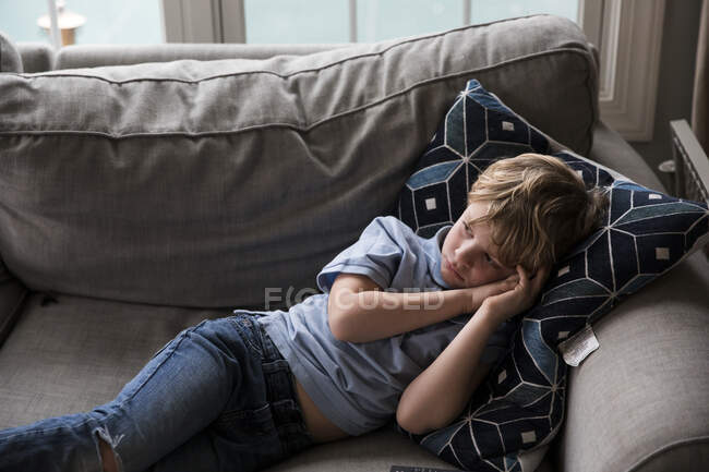 Trauriger blonder Junge schaut Fernsehen, während er auf Couch liegt — Stockfoto