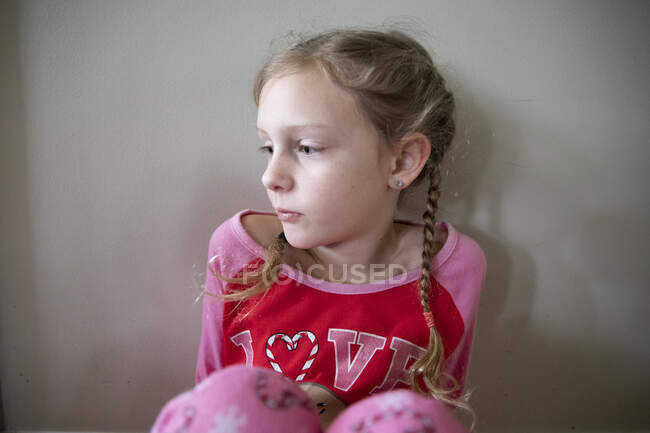 Menina loira em tranças francesas em pijamas parece tristemente fora da câmera — Fotografia de Stock