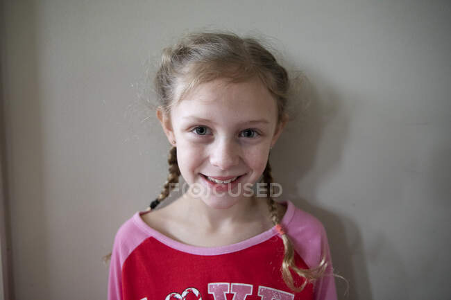 Chica rubia con trenzas francesas usando pijamas sonríe a la cámara - foto de stock