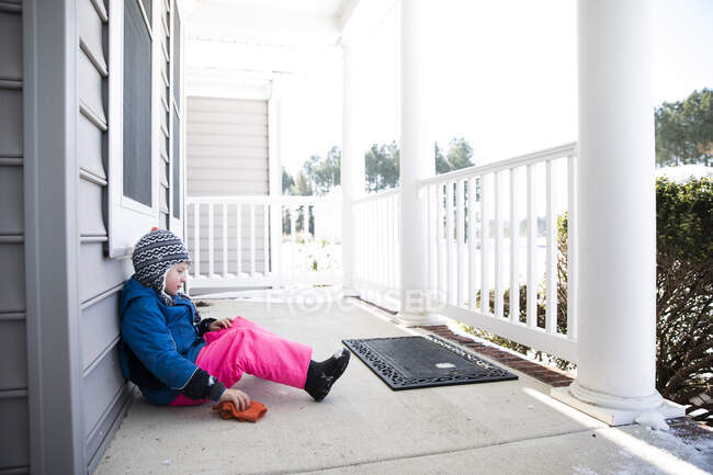 Вид мальчика в розовых снежных штанах, сидящего на заснеженном крыльце — стоковое фото