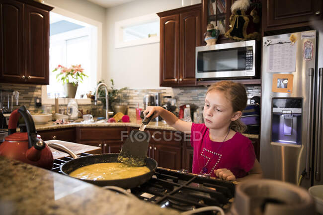 Freimütiges Bild eines lächelnden jungen Mädchens, das in einer unordentlichen Küche Eier kocht — Stockfoto