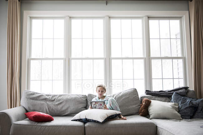 Wide View of Girl Home Sick From School On Couch With Tablet and Teddy — Stock Photo