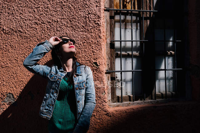 Junge Frau mit schwarzen Haaren trägt Sonnenbrille in der Nähe eines zerstörten Hauses — Stockfoto