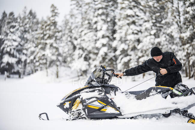 Hombre mayor comenzando moto de nieve con cordón de tracción. - foto de stock