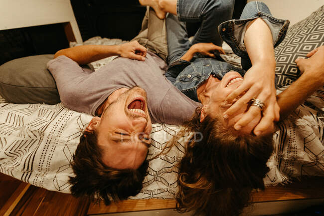 Engaged couple relax and laugh lying upside down on their van bed — Stock Photo