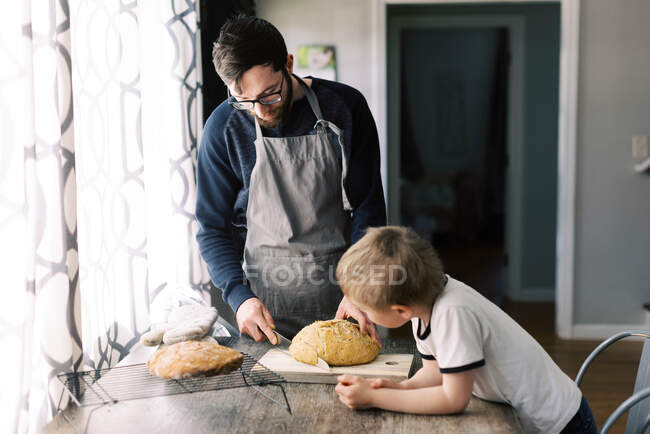 Vater und Sohn schneiden gemeinsam das selbstgebackene Brot auf dem Küchentisch. — Stockfoto