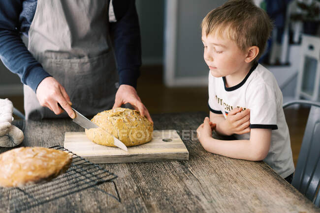 Vater und Sohn schneiden gemeinsam das selbstgebackene Brot auf dem Küchentisch. — Stockfoto