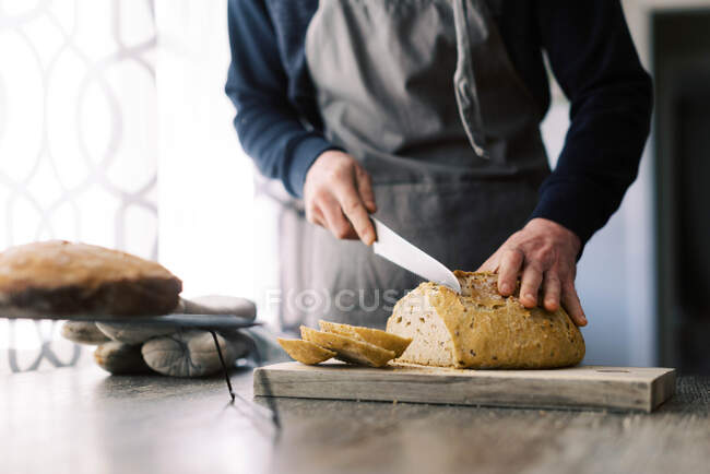 Человек режет хлеб ножом на белом фоне — стоковое фото