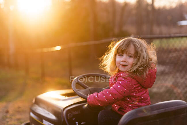 Uma menina de dois anos fingindo dirigir um cortador de grama. — Fotografia de Stock