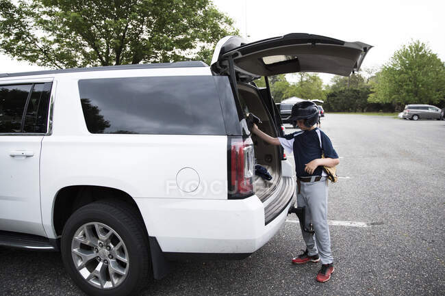 Хлопчик-підліток одягнений бейсбольний шолом завантажує обладнання в позашляховик після гри — стокове фото