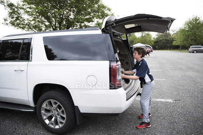 Teen Boy carga equipo de béisbol en la parte trasera de SUV blanco después del juego - foto de stock