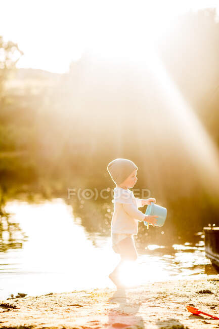 Été soleil doré bambin jouer avec seau au lac — Photo de stock