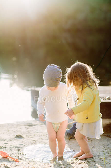 Niños pequeños pisando un charco en la playa en la arena durante la hora dorada - foto de stock