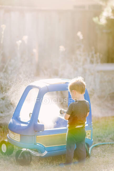Малыш моет игрушечную машину под летним солнцем — стоковое фото