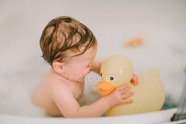 Baby in bath playing with big rubber duck — Stock Photo
