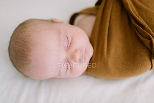 Primer plano del bebé recién nacido durmiendo en una envoltura marrón - foto de stock