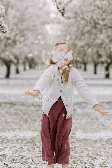 Junges Mädchen wirft in einem Mandelgarten Blütenblätter in die Kamera — Stockfoto