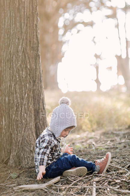 Toddler boy sitting against a tree in the woods — Stock Photo