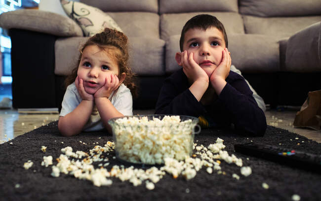 Hermanos viendo una película casera mientras comen palomitas de maíz - foto de stock