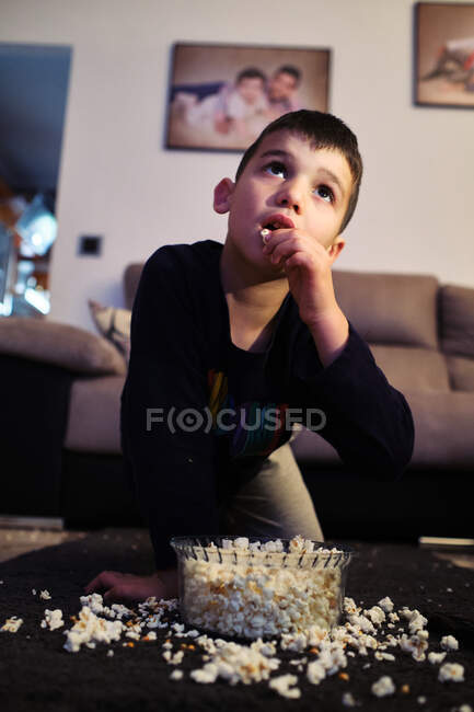 Uma criança come pipocas em casa enquanto assiste a um filme — Fotografia de Stock