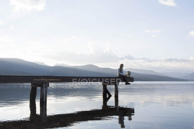 Eine Frau und ihr Hund genießen einen Abend auf dem Dock am Hebgener See. — Stockfoto