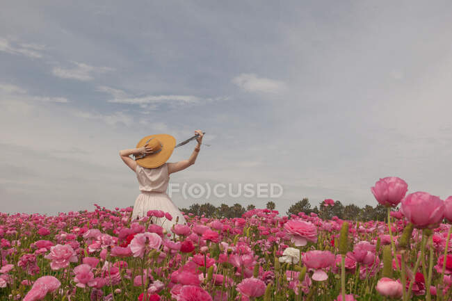 Junge Frau im Kleid mit Hut auf einem Hintergrund aus Blumen — Stockfoto