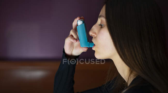 Mulher inalando um inalador de asma azul em casa. — Fotografia de Stock