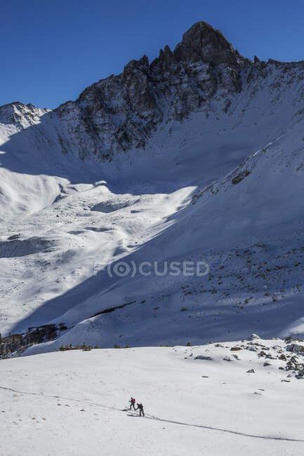 Two people backcountry ski amid jagged peaks in Colorado. — Stock Photo