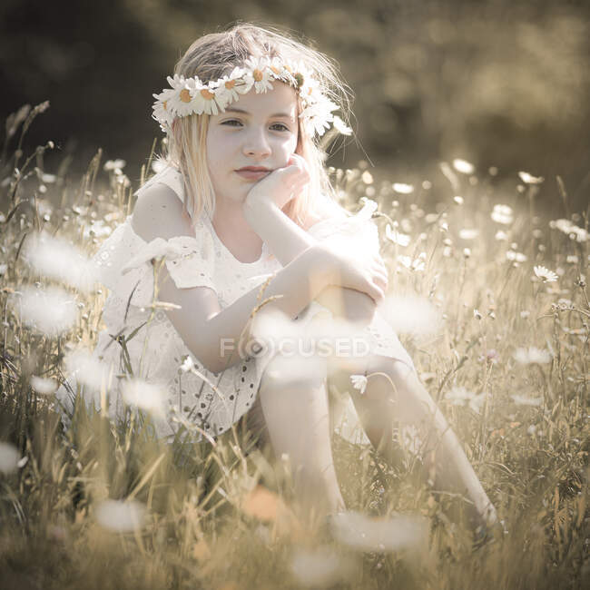 Girl with a melancholy look, sitting in a field with lots of flowers — Stock Photo