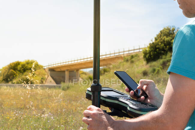Vermessungsingenieur mit GPS-Gerät, der die Daten mit seinem Smartphone überprüft — Stockfoto