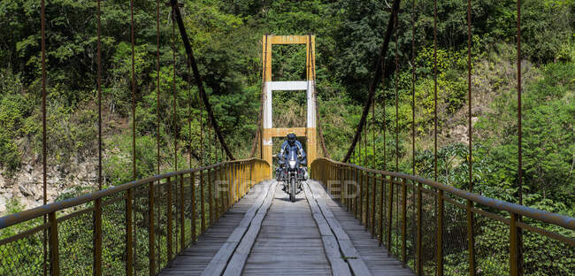 Homme conduisant une moto de tourisme sur un pont suspendu au Pérou — Photo de stock