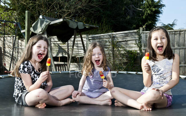 Three girls eating popsicles on trampoline in Woking - England — Stock Photo