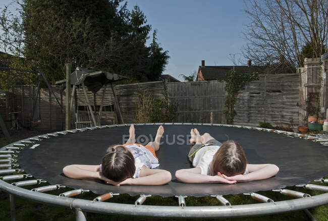 Dos chicas jóvenes relajándose en el trampolín en Woking - Inglaterra - foto de stock