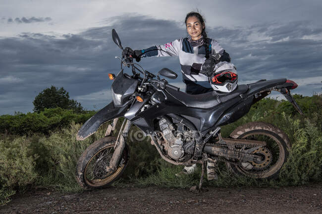 Mulher posando atrás de sua moto super motocicleta estilo na estrada de terra — Fotografia de Stock