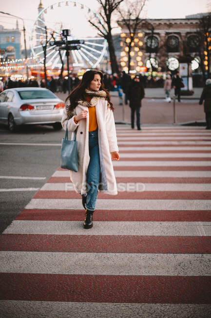 Menina adolescente pensativo em roupas quentes cruzando estrada na cidade no inverno — Fotografia de Stock