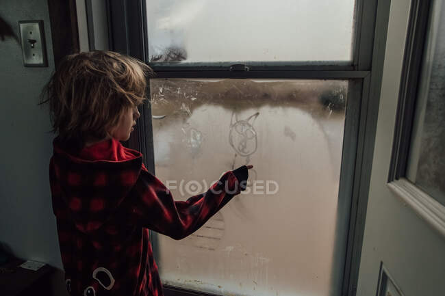Little boy drawing a picture on the window condensation — Stock Photo