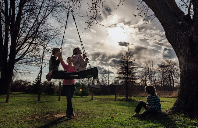 Crianças brincando fora em um baloiço de pneu ao pôr do sol — Fotografia de Stock