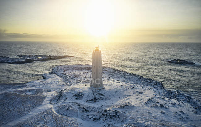 Drone vista da torre de pedra do farol no fundo da magnífica paisagem marinha e terreno nevado durante o pôr do sol — Fotografia de Stock