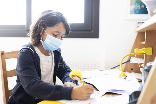 Молодой испанский мальчик делает домашнюю работу в маске — стоковое фото