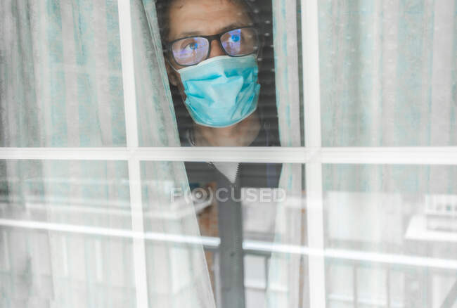 Середній чоловік у медичній масці під карантином у лікарні, притиснутий до вікна чолом. — стокове фото