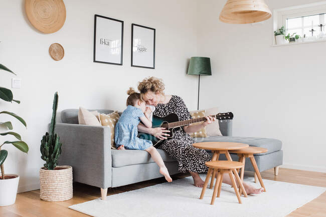 Madre e hija abrazándose mientras tocan la guitarra en casa - foto de stock