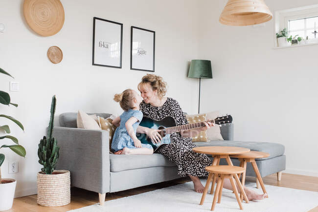 Madre e figlia seduti a suonare la chitarra insieme ridendo a casa — Foto stock
