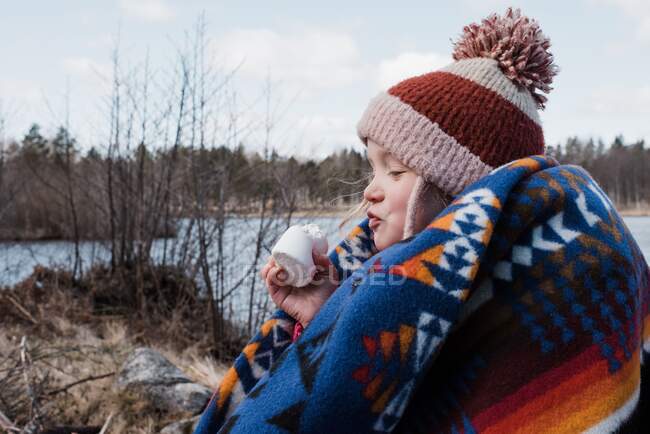 Young girl wrapped in a blanket eating a marshmallow whilst camping — Stock Photo