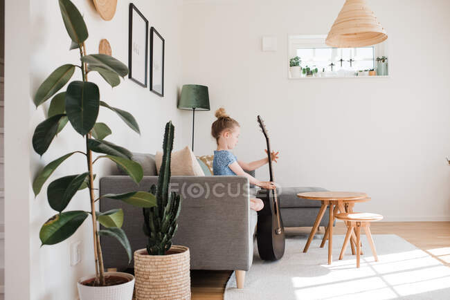 Young girl holding a guitar, musical instrument whilst sat at home — Stock Photo