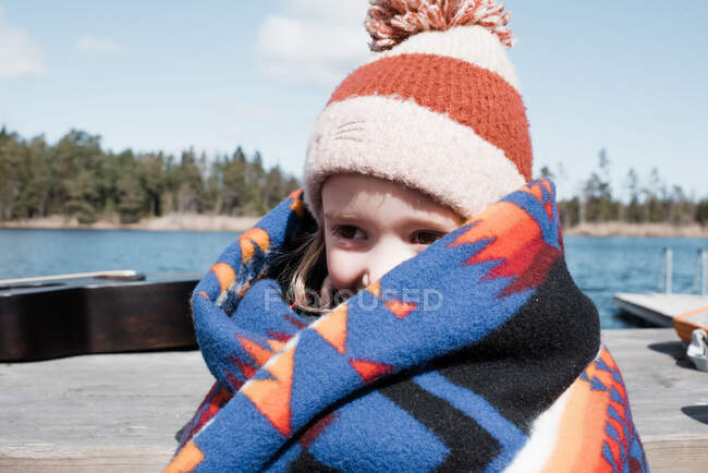 Молода дівчина, загорнута в ковдру біля озера, зберігає тепло — стокове фото