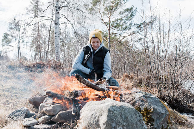 Uomo seduto accanto a un fuoco all'aperto durante il campeggio — Foto stock