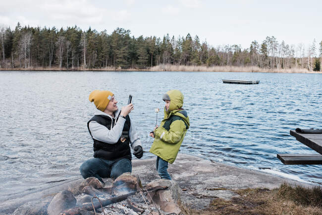Man taking a picture of his son whilst camping eating marshmallows — Stock Photo