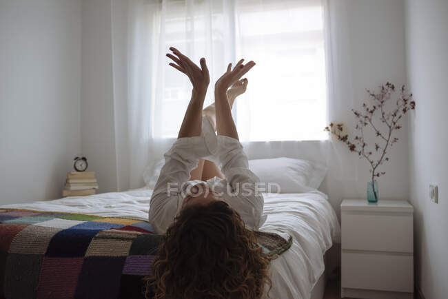 Femme aux cheveux bouclés couchée au lit jouant avec ses mains — Photo de stock